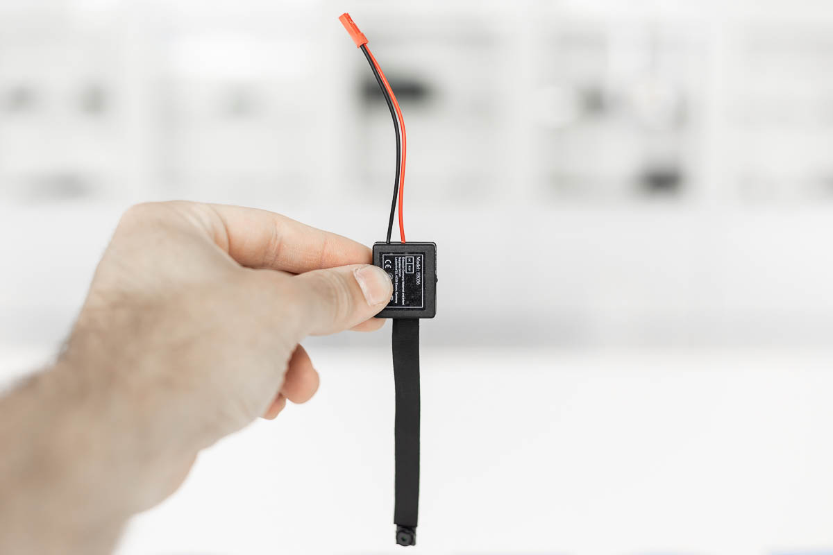 Microtelecamera spia con DVR e cavo flat nero tenuta in mano per mostrare dimensioni ridotte – CAM.04